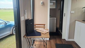 Ein kleines Zimmer mit Holztisch, Stuhl, einer kleinen Küchenzeile und Blick auf ein blaues Auto vor dem Fenster.