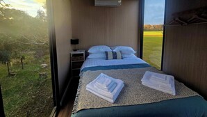 Ein Schlafzimmer mit Bett, Nachttisch, Klimaanlage und Blick auf ein grünes Feld.