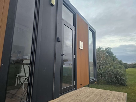 A modern, compact building with large glass doors, a wooden deck, and a sign indicating a restaurant or cafe.. Mikkira Koala Cabin by Tiny Away
