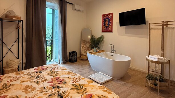 Una camera da letto con un letto grande, una vasca da bagno, una televisione e un balcone.