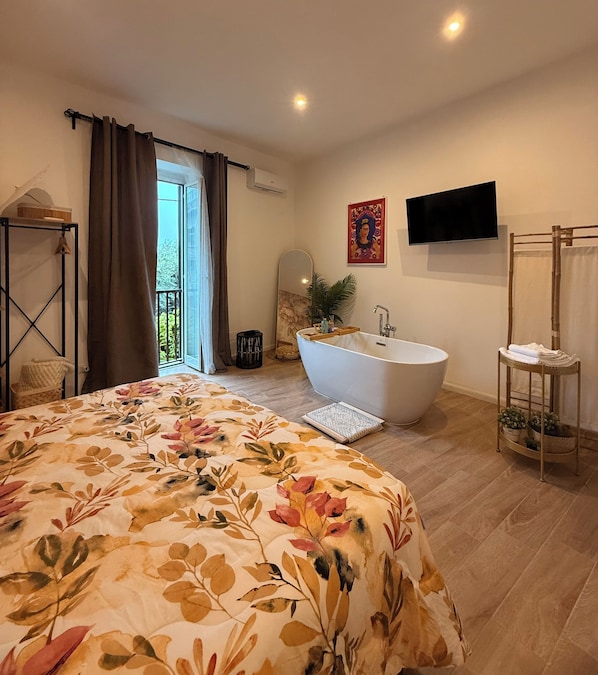 Une chambre avec un grand lit, une baignoire, une télévision et un balcon.
