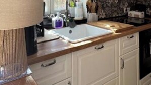 Una cucina moderna con mobili bianchi, un piano di lavoro in legno, un lavello e una cappa aspirante nera.