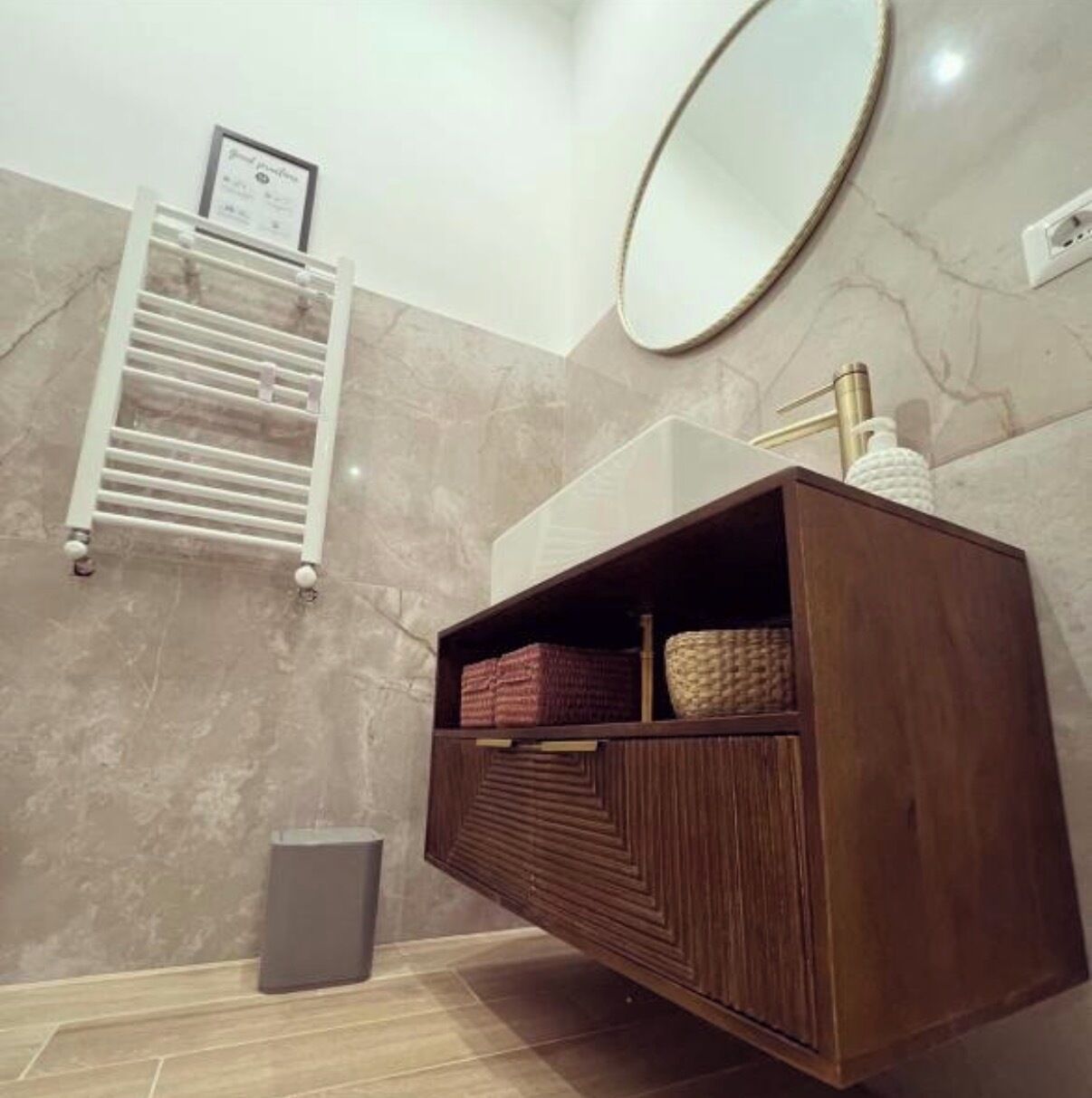 A bathroom with a wooden vanity, a towel rack, a mirror, and a trash bin.