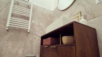 A bathroom with a wooden vanity, a towel rack, a mirror, and a trash bin.
