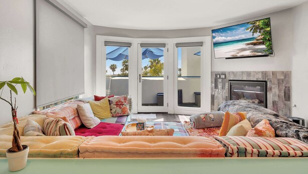 A living room with a sofa, a potted plant, and a flat-screen TV on the wall. - Santorini Escape in La Jolla! | Walk to the Beach (San Diego)