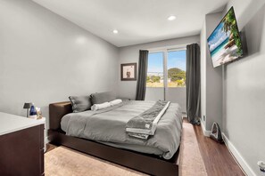 A modern bedroom with a bed, a desk, a flat-screen TV, and a view of the outdoors. - Santorini Escape in La Jolla! | Walk to the Beach (San Diego)