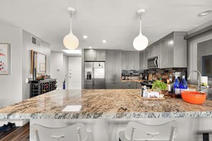 A modern kitchen with granite countertops, stainless steel appliances, and pendant lighting. - Santorini Escape in La Jolla! | Walk to the Beach (San Diego)