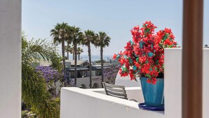 A balcony with a chair, a potted plant with red flowers, and a view of palm trees and buildings. - Santorini Escape in La Jolla! | Walk to the Beach (San Diego)