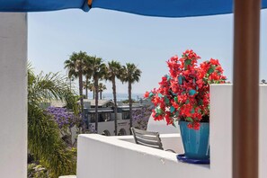 A balcony with a chair, a potted plant with red flowers, and a view of palm trees and buildings. - Santorini Escape in La Jolla! | Walk to the Beach (San Diego)