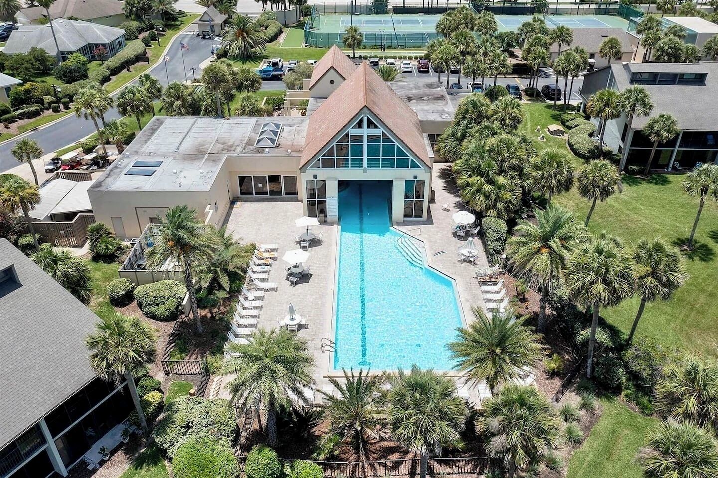 Un hotel amb piscina, palmeres i una pista de tennis al fons.