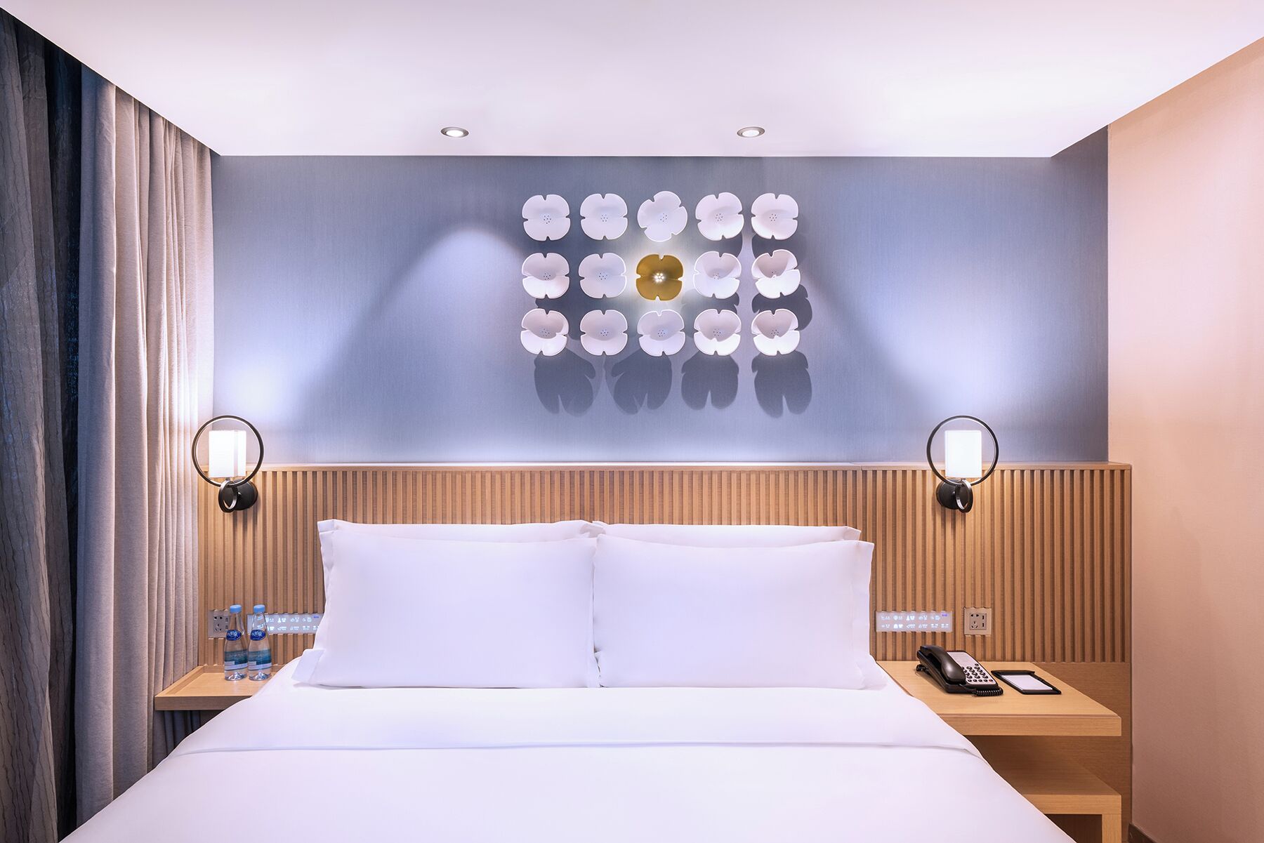 Ein Hotelzimmer mit einem Bett, zwei Nachttischen, einer Wandleuchte und einem dekorativen Wandbild.