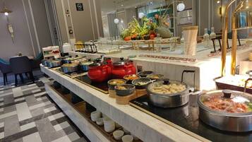 Un buffet avec différents récipients contenant de la nourriture, un espace avec des chaises où les gens peuvent s’asseoir, et une composition florale décorative.