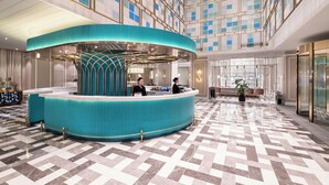 Et hotel lobby med en central receptionsdisk, en indtjekningsdisk og et siddeområde med en potteplante.