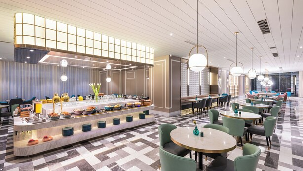 En moderne hotellobby med morgenmadsområde, siddepladser og en receptionsdisk.