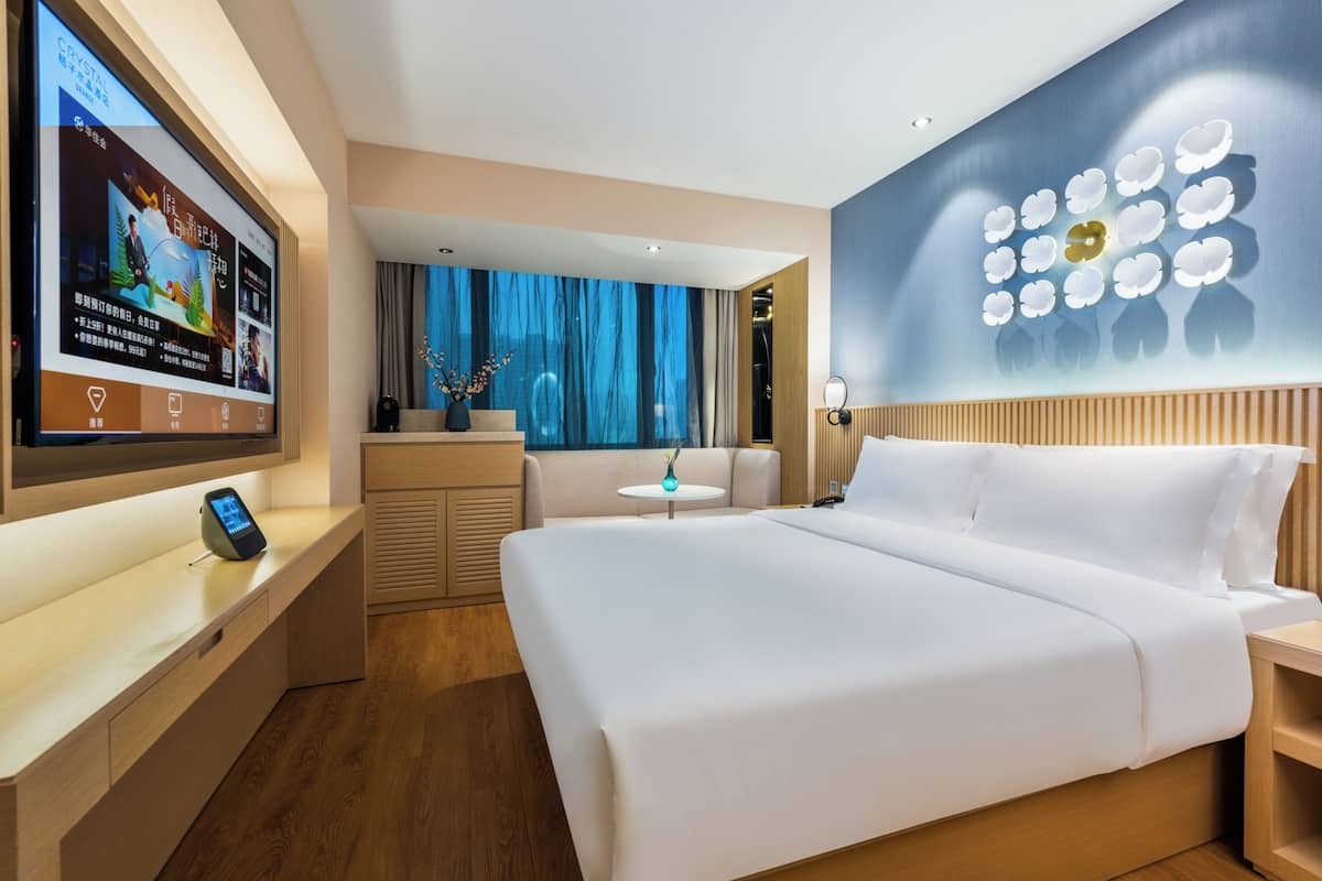 A modern hotel room with a large bed, a TV on the wall, a small table, and a decorative wall piece.