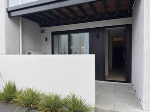 Un edificio moderno con un acceso cubierto, una entrada visible y un pequeño jardín con plantas.