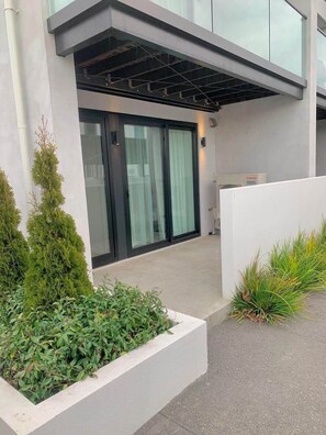 A modern building with a glass door entrance, a white exterior wall, and a small garden area with plants. - Best location in CBD Free parking (Christchurch)