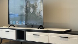 Un téléviseur à écran plat, posé sur un meuble multimédia moderne, avec une télécommande, un tiroir et une étagère.