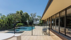 Een modern gebouw met een zwembad, terras en uitzicht op bomen en een gebouw in de verte.