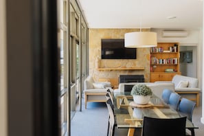 A modern living room with a glass dining table, sofas, a fireplace, a TV, and a bookshelf. - Manager's House - 4 Bedroom House (Yarra Glen)
