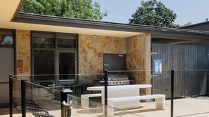 Een terras buiten met een barbecue, zitplaatsen en een televisie.