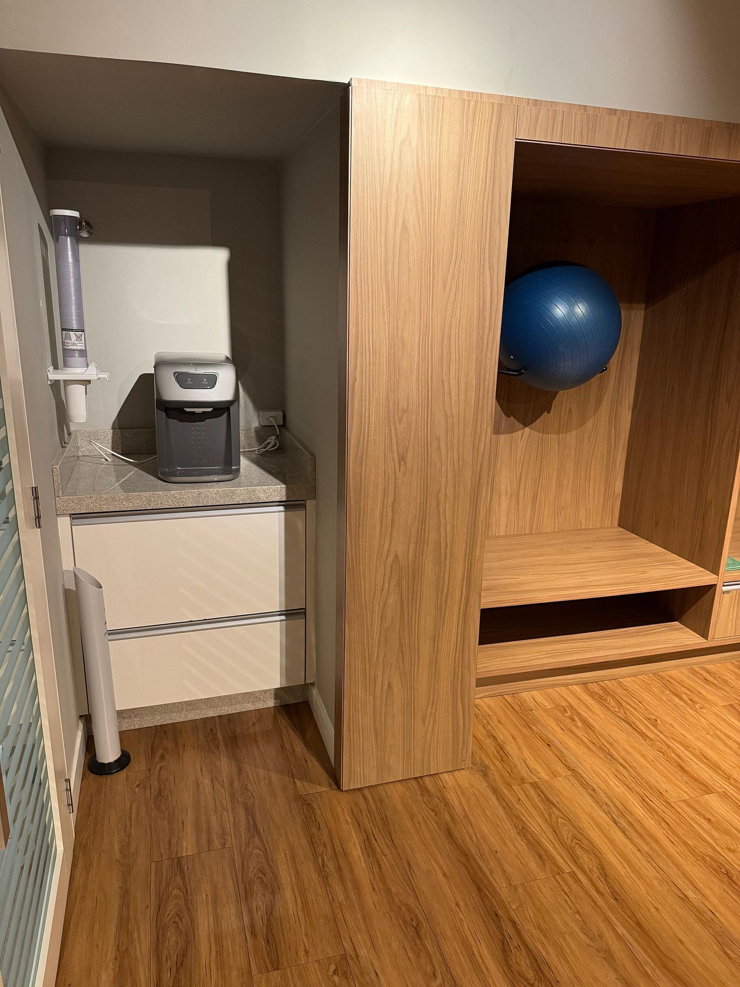 Quarto compacto com cozinha compacta, incluindo cafeteira e dispensador de água.