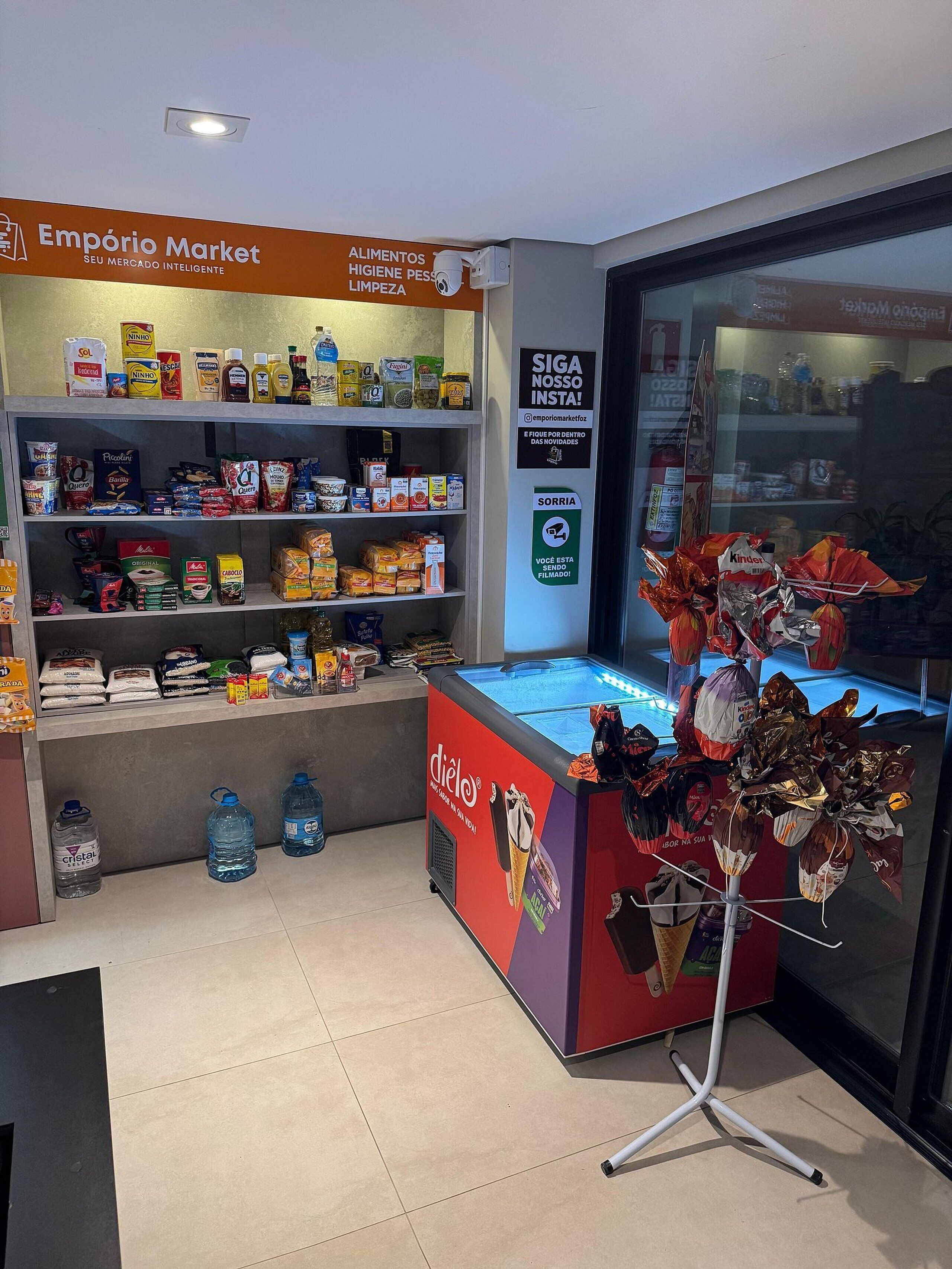 A retail space with shelves stocked with various food items, a freezer with ice cream, and a security camera.