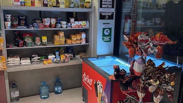 A retail space with shelves stocked with various food items, a freezer with ice cream, and a security camera.