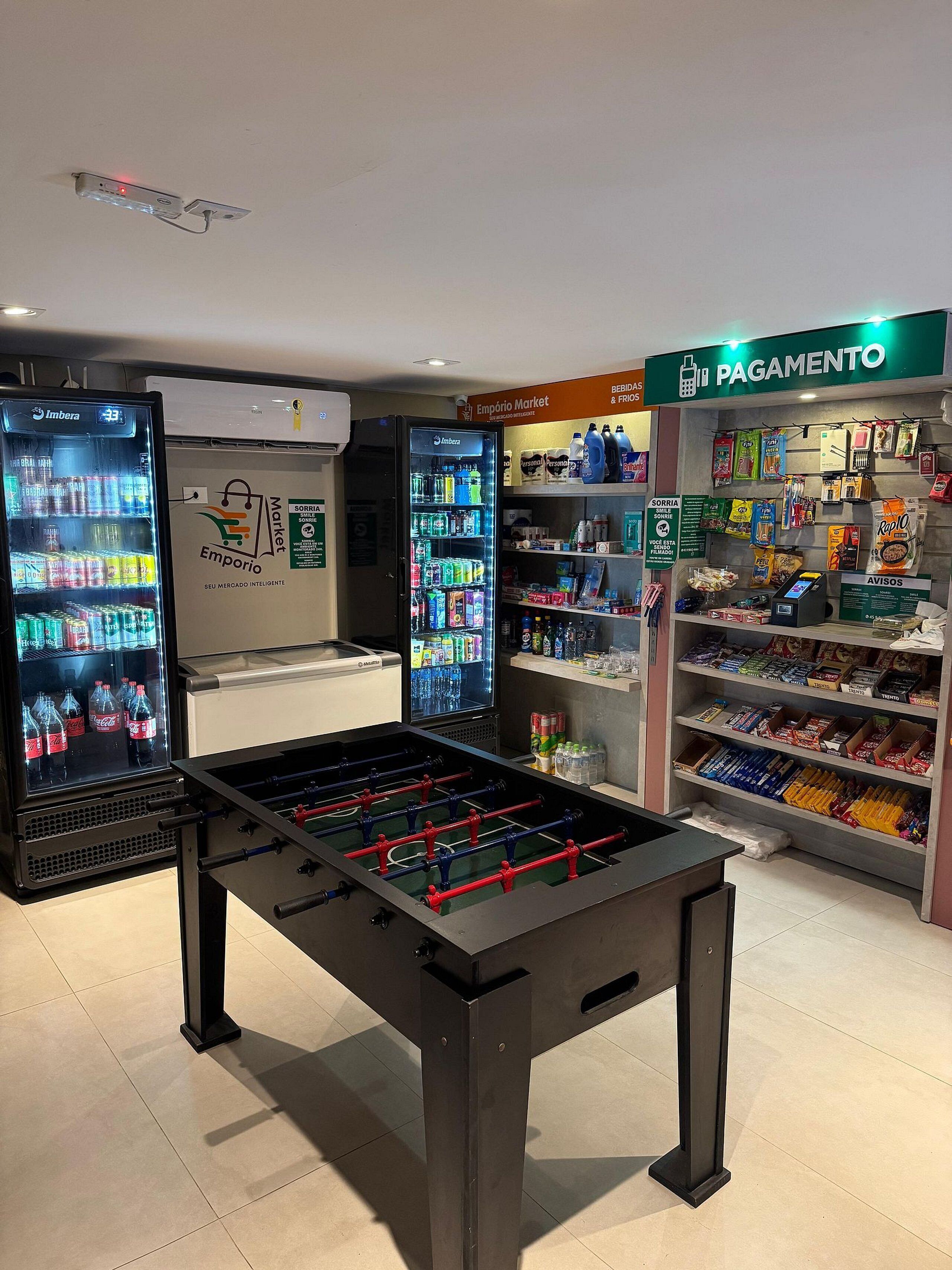 Um quarto com mesa de futebol de mesa, máquinas de venda automática e prateleiras cheias de petiscos e bebidas.
