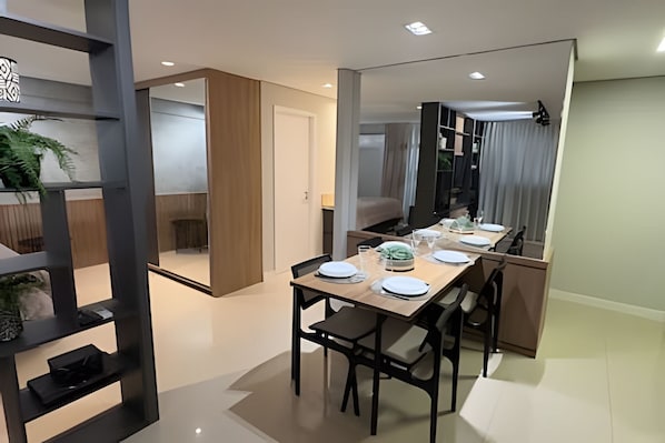 A modern dining area with a long table set for four, a mirror reflecting the room, and a plant on a shelf. - Casa Confortavel em Foz do Iguaçu (Foz do Iguaçu)