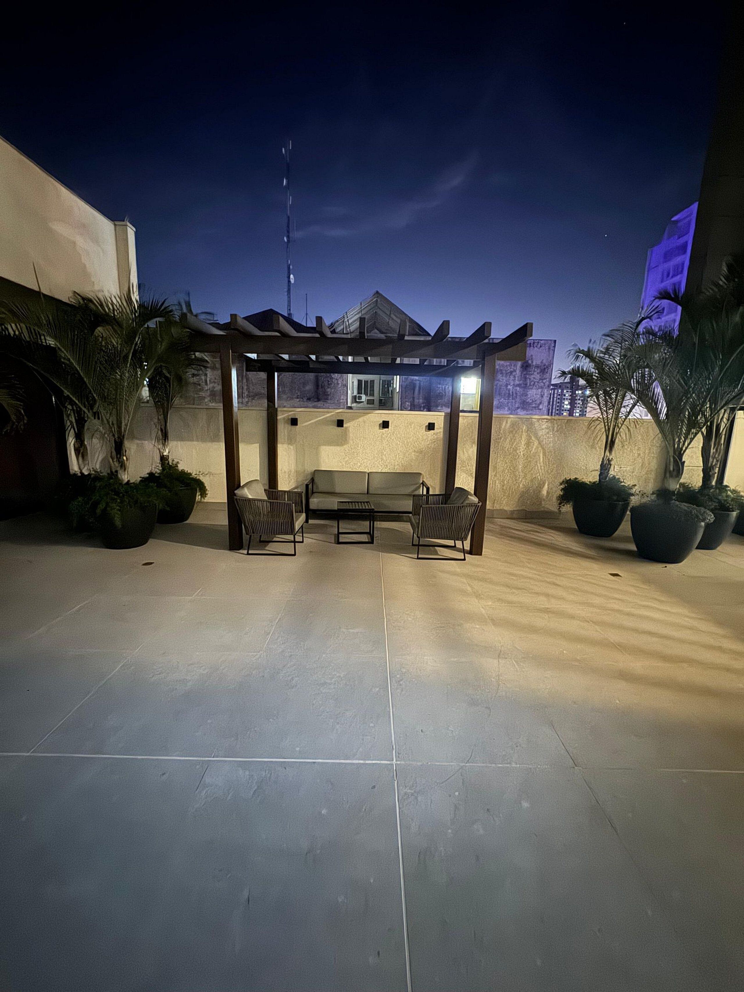 Un patio al aire libre con una pérgola de madera, asientos y plantas en macetas.