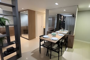A modern dining area with a long table set for four, a mirror reflecting the room, and a plant on a shelf. - Casa Confortavel em Foz do Iguaçu (Foz do Iguaçu)