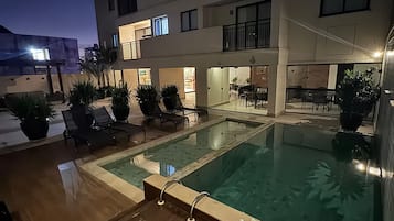 Et poolområde med træterrasse, liggestole og krukker med planter.