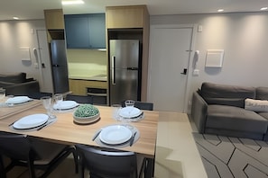 Un comedor moderno con una mesa de madera dispuesta para cuatro personas, un sofá gris y una cocina al fondo.