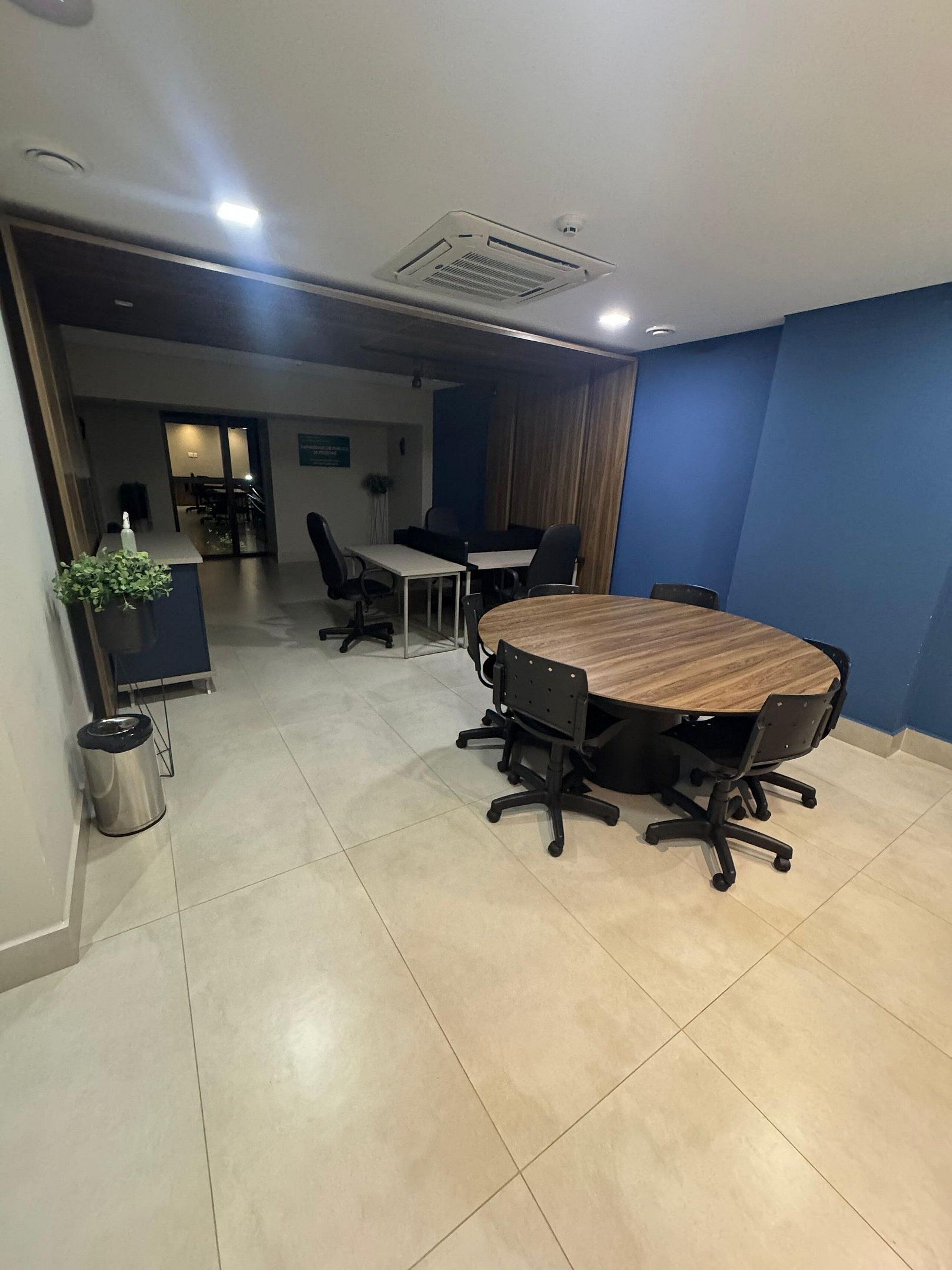 Uma sala de conferência com uma grande mesa redonda, cadeiras de escritório pretas e um vaso de planta.