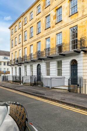 A multi-story building with a yellow facade, black iron railings, and white windows. - Stunning 2 Bedroom Flat in the Centre of Cheltenham (Cheltenham)