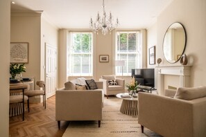 A living room with a fireplace, a television, and a chandelier. - Stunning 2 Bedroom Flat in the Centre of Cheltenham (Cheltenham)