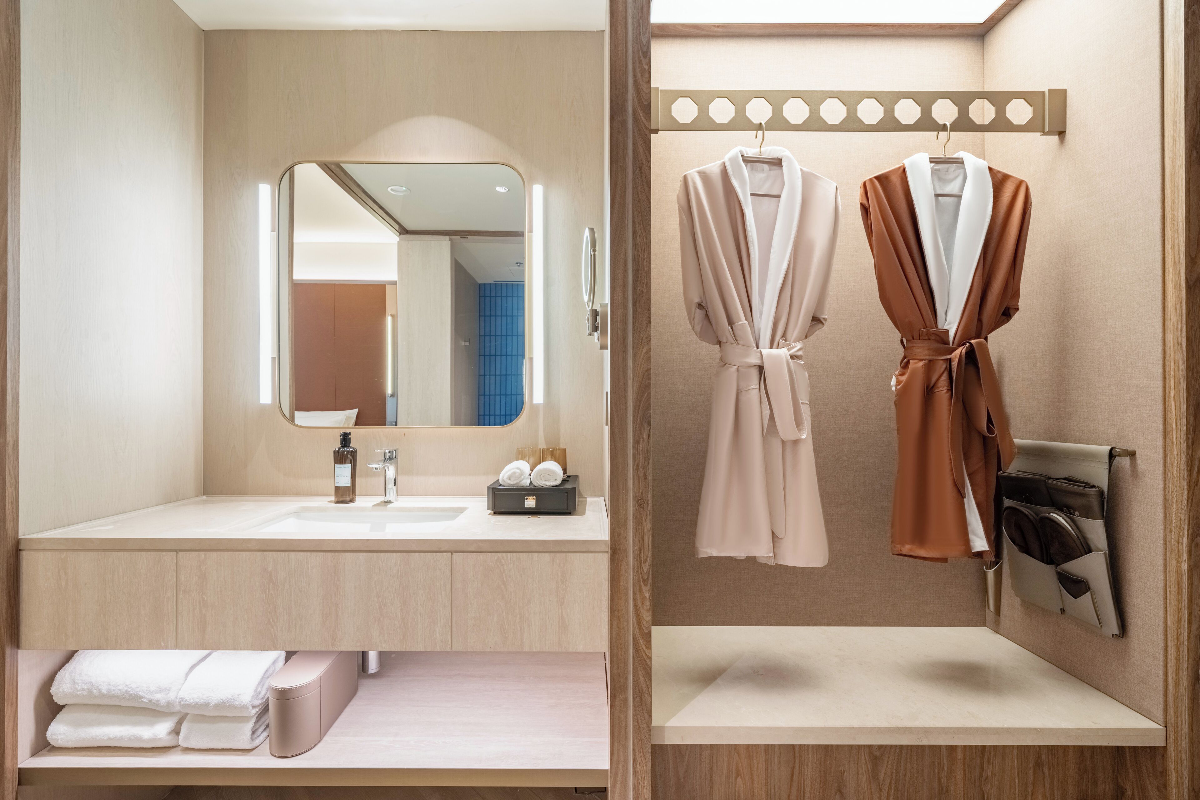 A modern bathroom with a large mirror, two sinks, a towel rack with robes, and a towel bar.