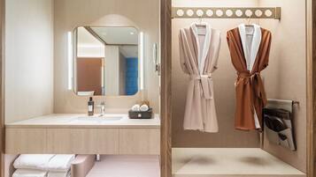 A modern bathroom with a large mirror, two sinks, a towel rack with robes, and a towel bar.