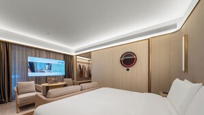 Una habitación de hotel moderna con una cama grande, un sofá, una pequeña mesa y una pantalla de televisión mostrando una vista de la habitación.