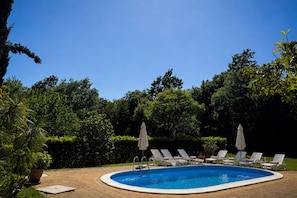 Ein Schwimmbecken mit Liegestühlen und Sonnenschirmen, umgeben von viel Grün.