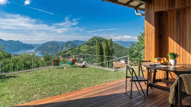 Eine Holzterrasse mit Tisch und Stühlen, mit Blick auf eine malerische Landschaft mit Bergen und einem See.