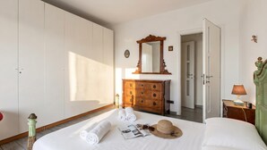 Et hotelværelse med en seng, en trækommode, et spejl, en dør og et natbord med en lampe.