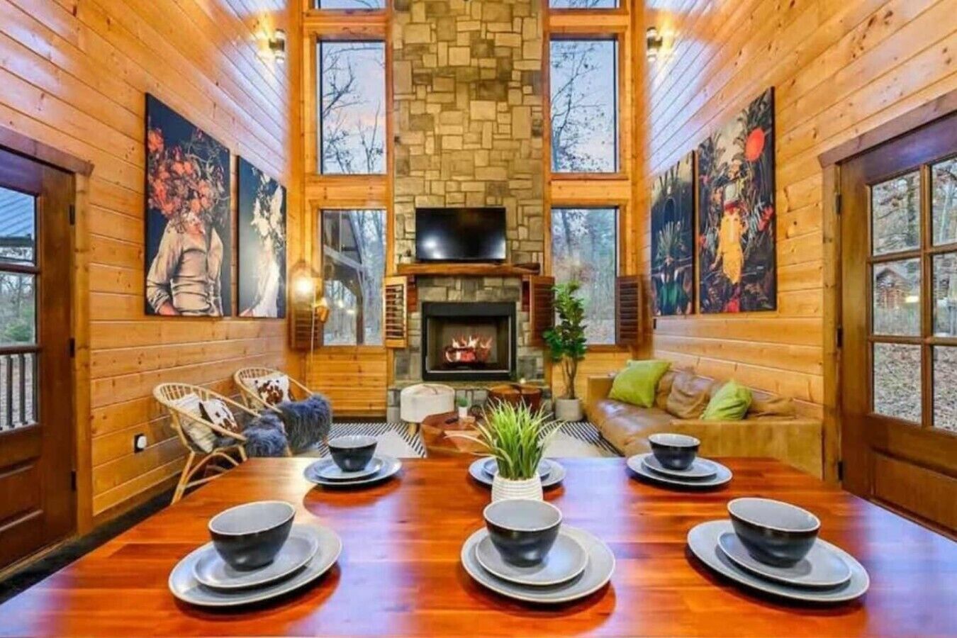 Interior de una cabaña de madera con chimenea, una mesa de comedor dispuesta con cuencos y platos, y un sofá con cojines.