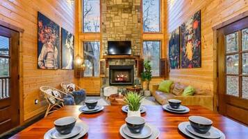 Interior de una cabaña de madera con chimenea, una mesa de comedor dispuesta con cuencos y platos, y un sofá con cojines.