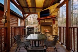 A wooden deck with a stone fireplace, a table, and chairs. - Walk to Hochatown, Hot Tub, Pool Table + Bunk Loft (Broken Bow)