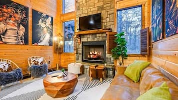 Interior acogedor de una cabaña con chimenea de piedra, paredes de madera y ventanas amplias.