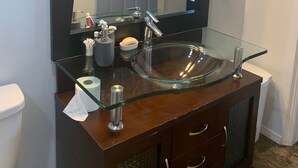 A bathroom with a glass sink, a dark wooden vanity, a large mirror, and a ceiling light fixture. - One Bedroom Basement apartment on Red River bank (Selkirk)