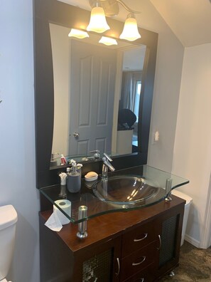 A bathroom with a glass sink, a dark vanity, a mirror, and a ceiling light fixture. - One Bedroom Basement apartment on Red River bank (Selkirk)