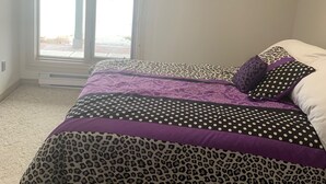 A bedroom with a large bed, a window with blinds, and a view of a snowy landscape. - One Bedroom Basement apartment on Red River bank (Selkirk)